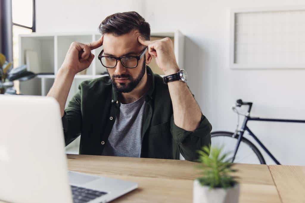 A man in front of a laptop, seemingly thinking about an important decision