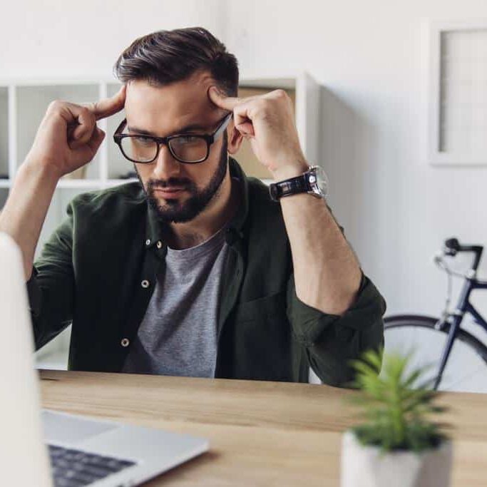 A man in front of a laptop, seemingly thinking about an important decision